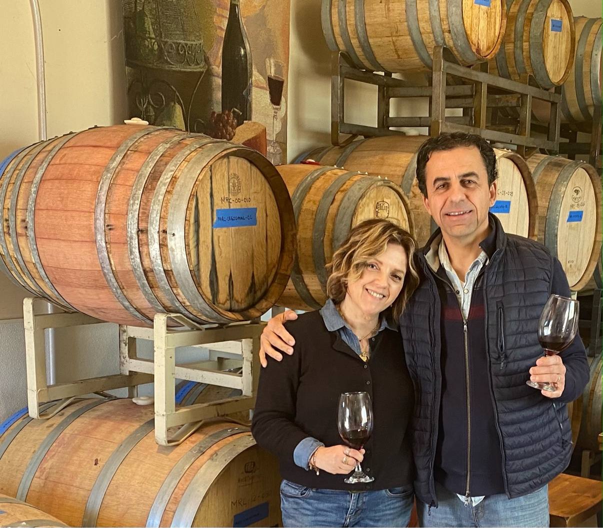Guillermo Seta sharing a glass with a smiling guest among the oak barrels