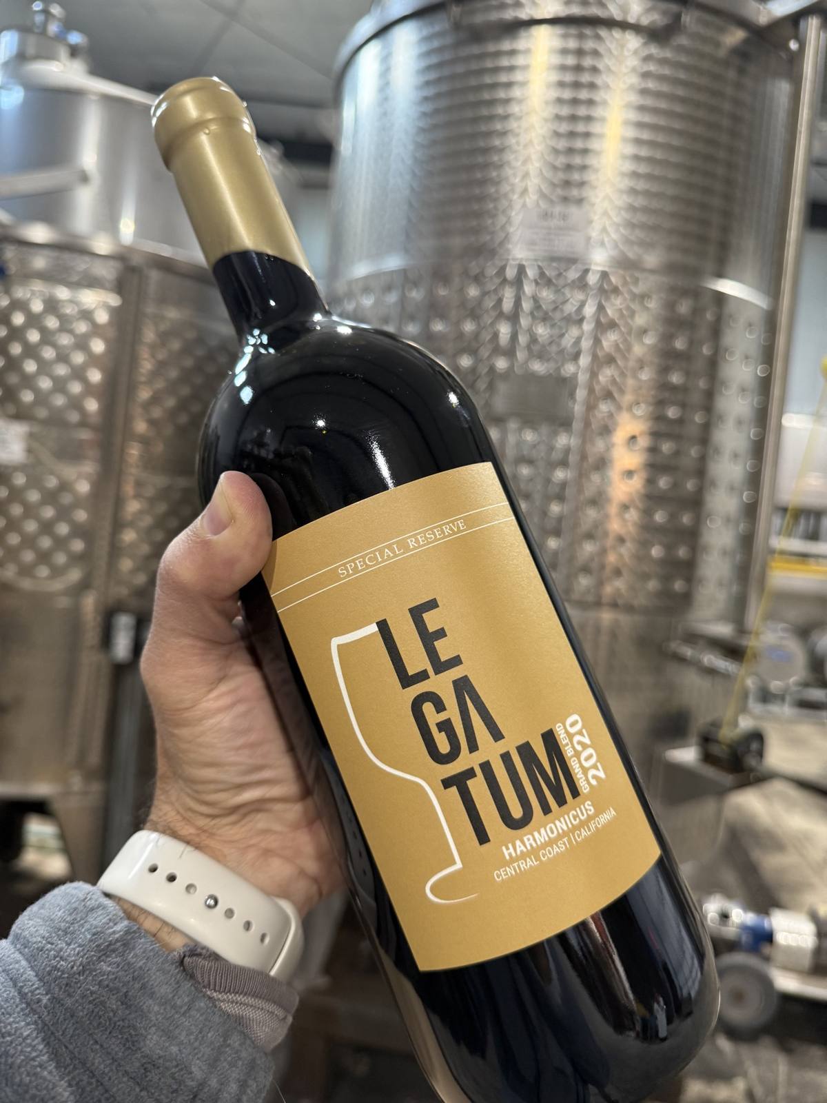 Legatum 2020 Harmonicus Special Reserve held in hand against stainless winery tanks