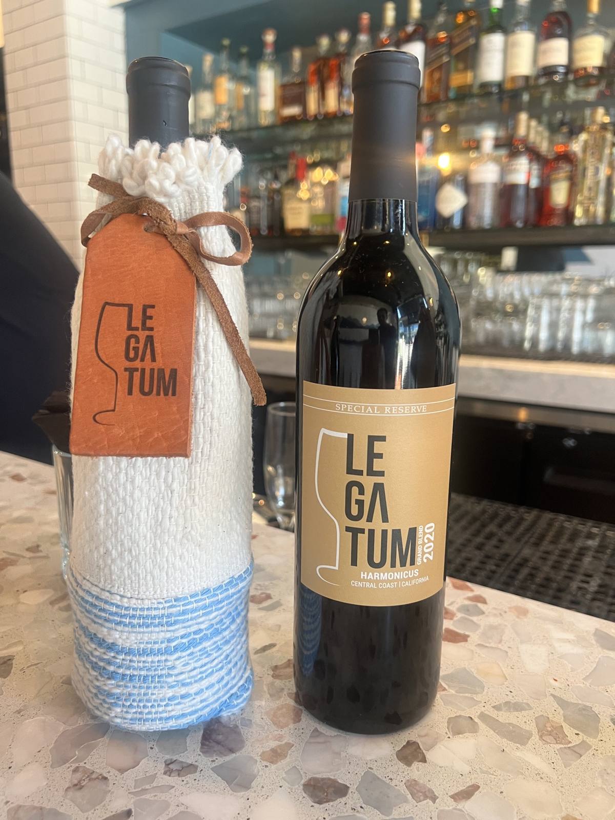 Gold-label 2020 Harmonicus Special Reserve beside the white hand-woven sleeve and leather tag at a bar