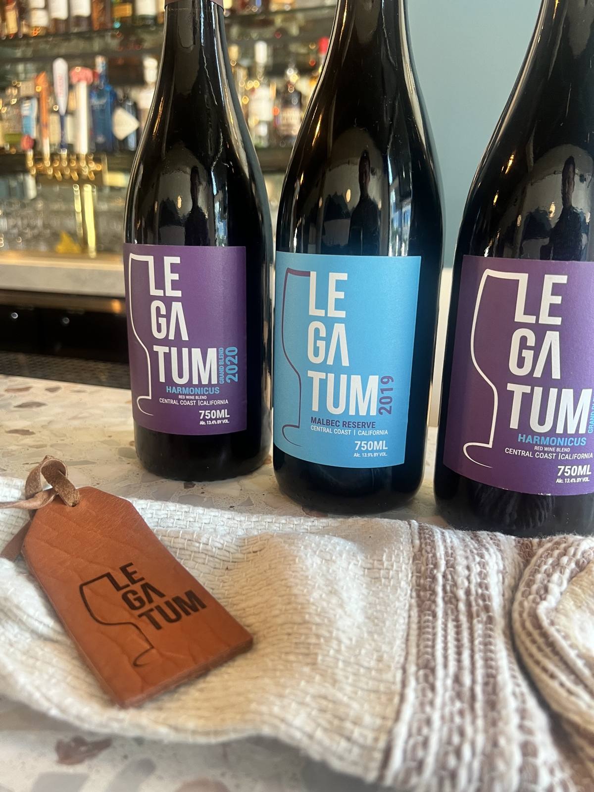 Close arrangement of purple-label Harmonicus, blue-label Malbec Reserve, woven sleeve, and leather tag