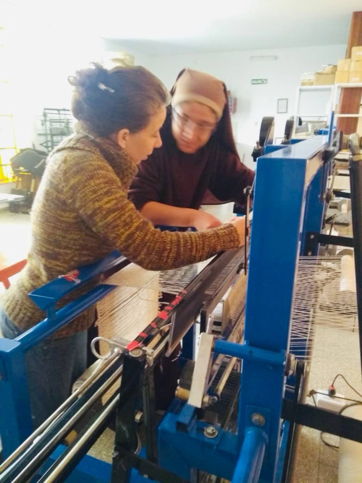 Two women of El Refugio working together at a blue textile loom