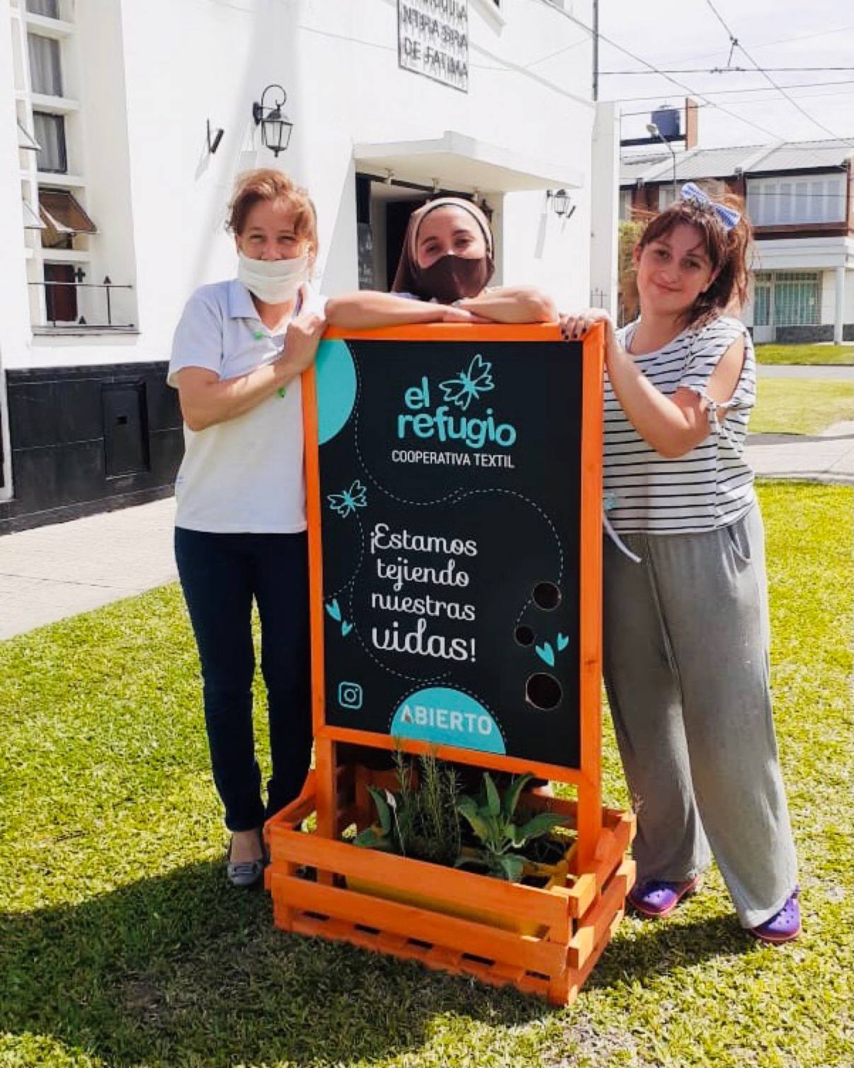 Three women of El Refugio beside the cooperative sign reading Estamos tejiendo nuestras vidas