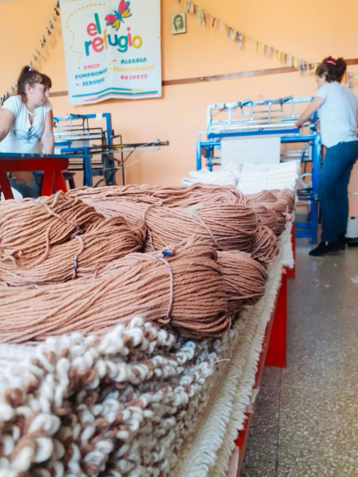 El Refugio workshop with yarn, looms, and its values banner
