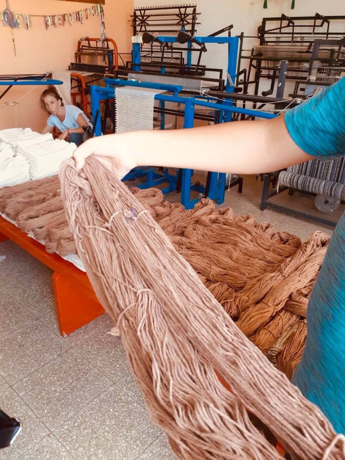 A hand holding skeins of warm brown yarn inside the textile workshop