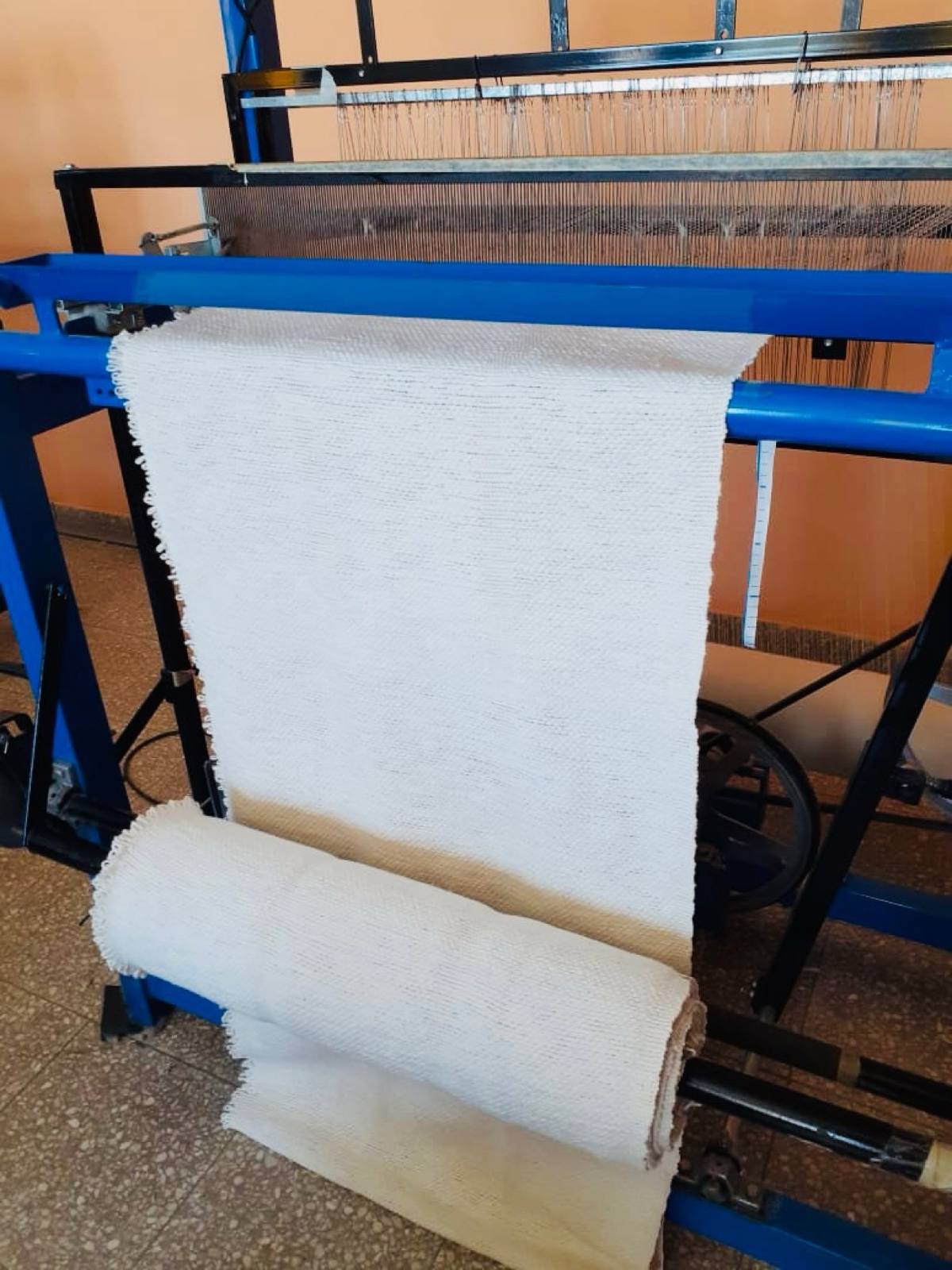 White woven fabric emerging from a blue loom