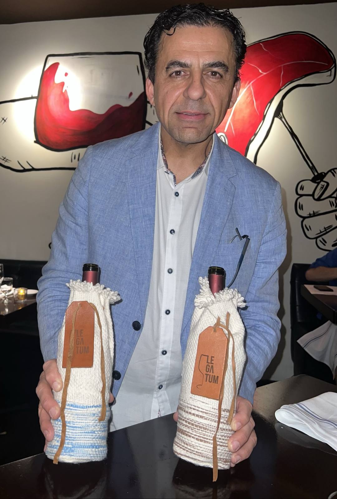 Guillermo Seta holding two bottles dressed in hand-woven sleeves with leather Legatum tags