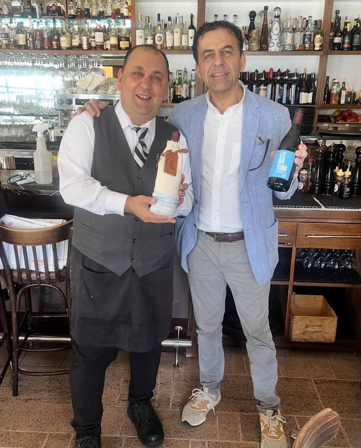 Guillermo Seta and a member of the Il Pastaio team holding Legatum bottles, including the woven-sleeve bottle