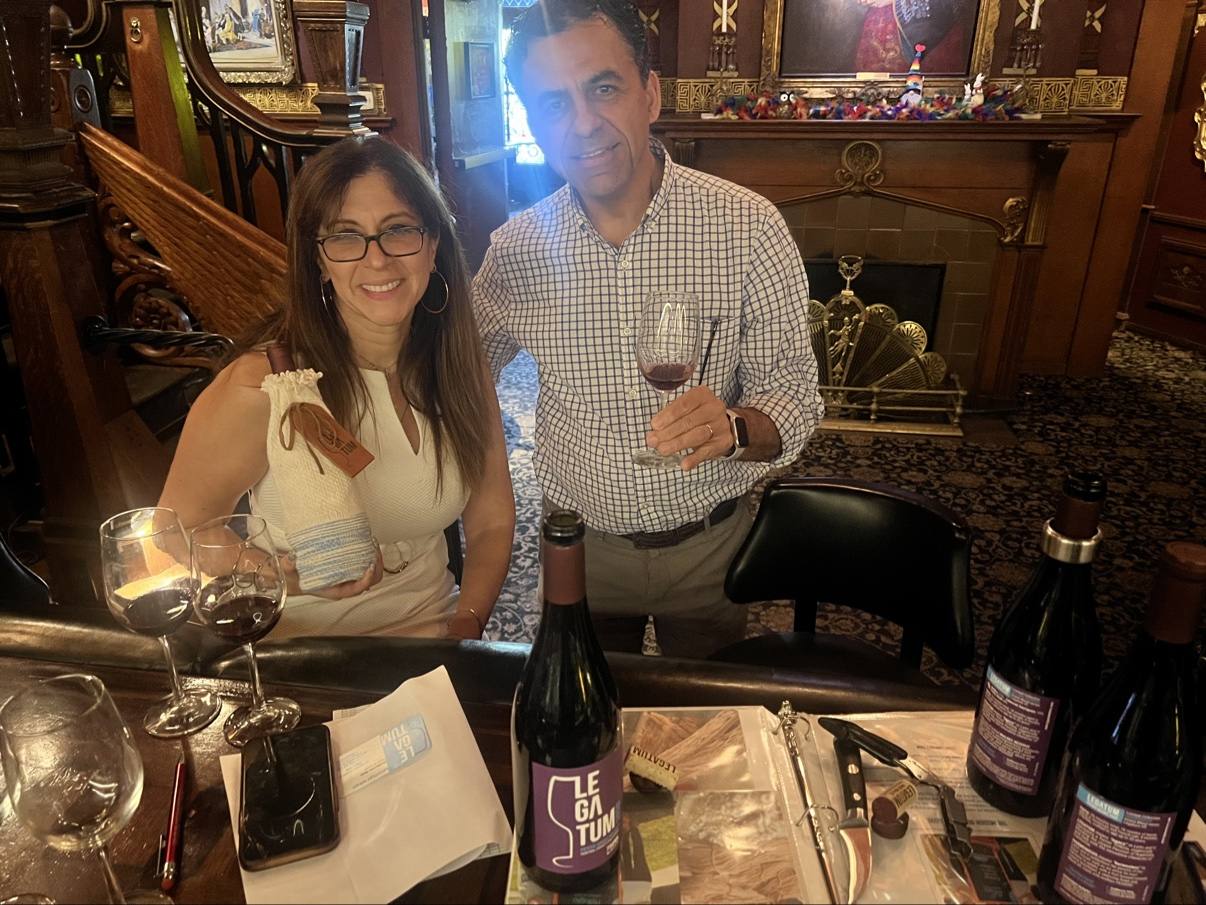 Guillermo Seta and a woman at a tasting table inside an ornate wood-paneled room, with Legatum bottles and a sleeved bottle