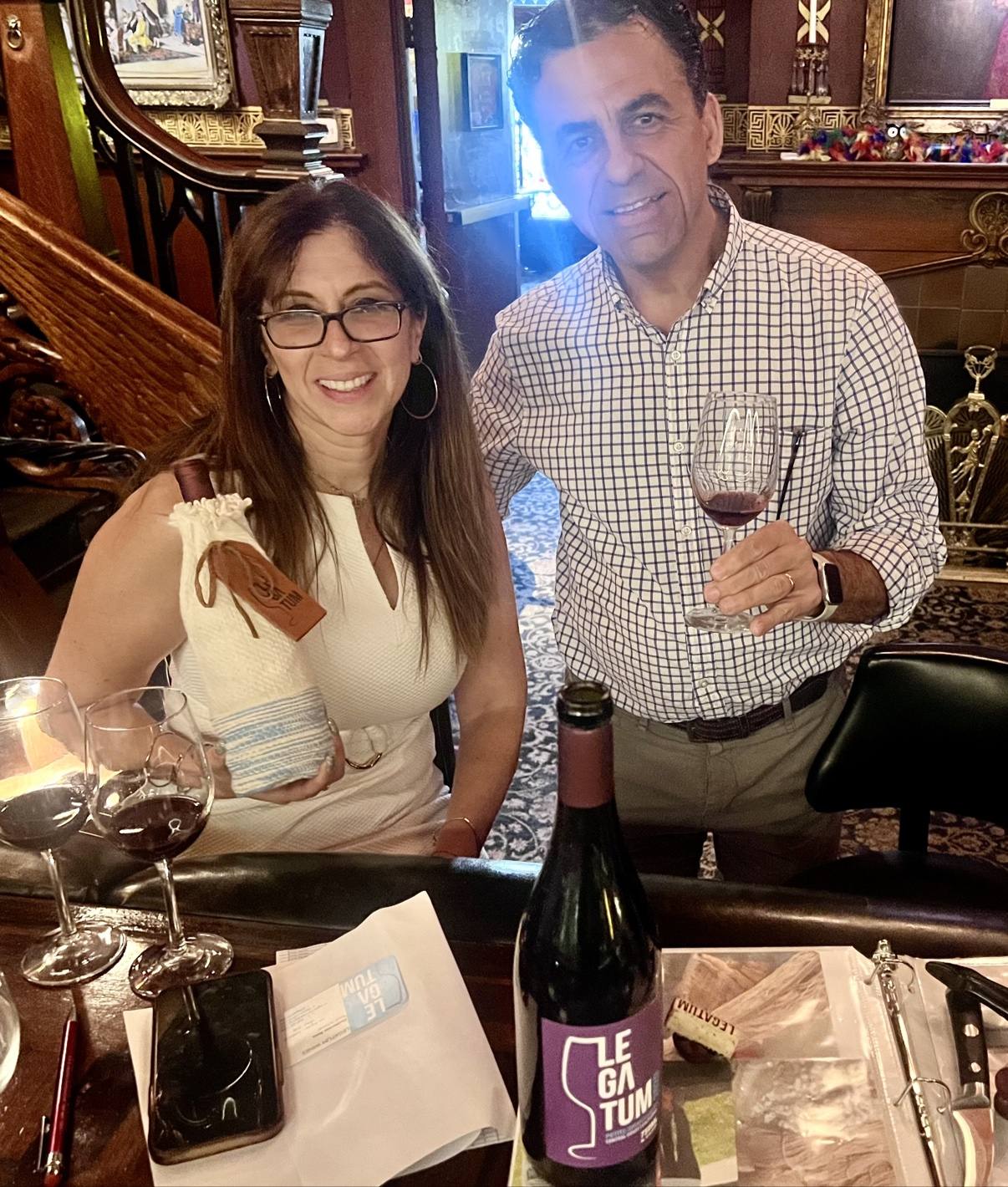 Guillermo Seta holding a glass beside a woman holding a sleeved Legatum bottle inside the Magic Castle