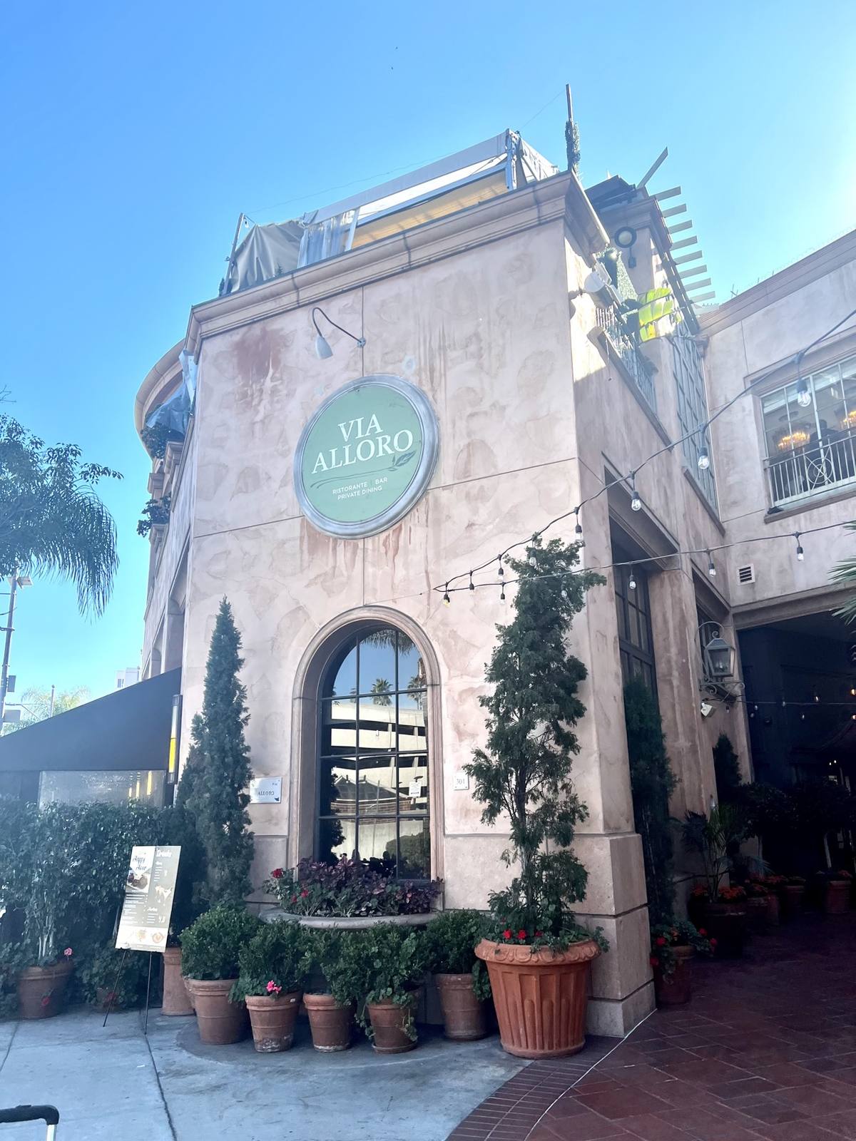 Green round Via Alloro sign on the pale stone restaurant building