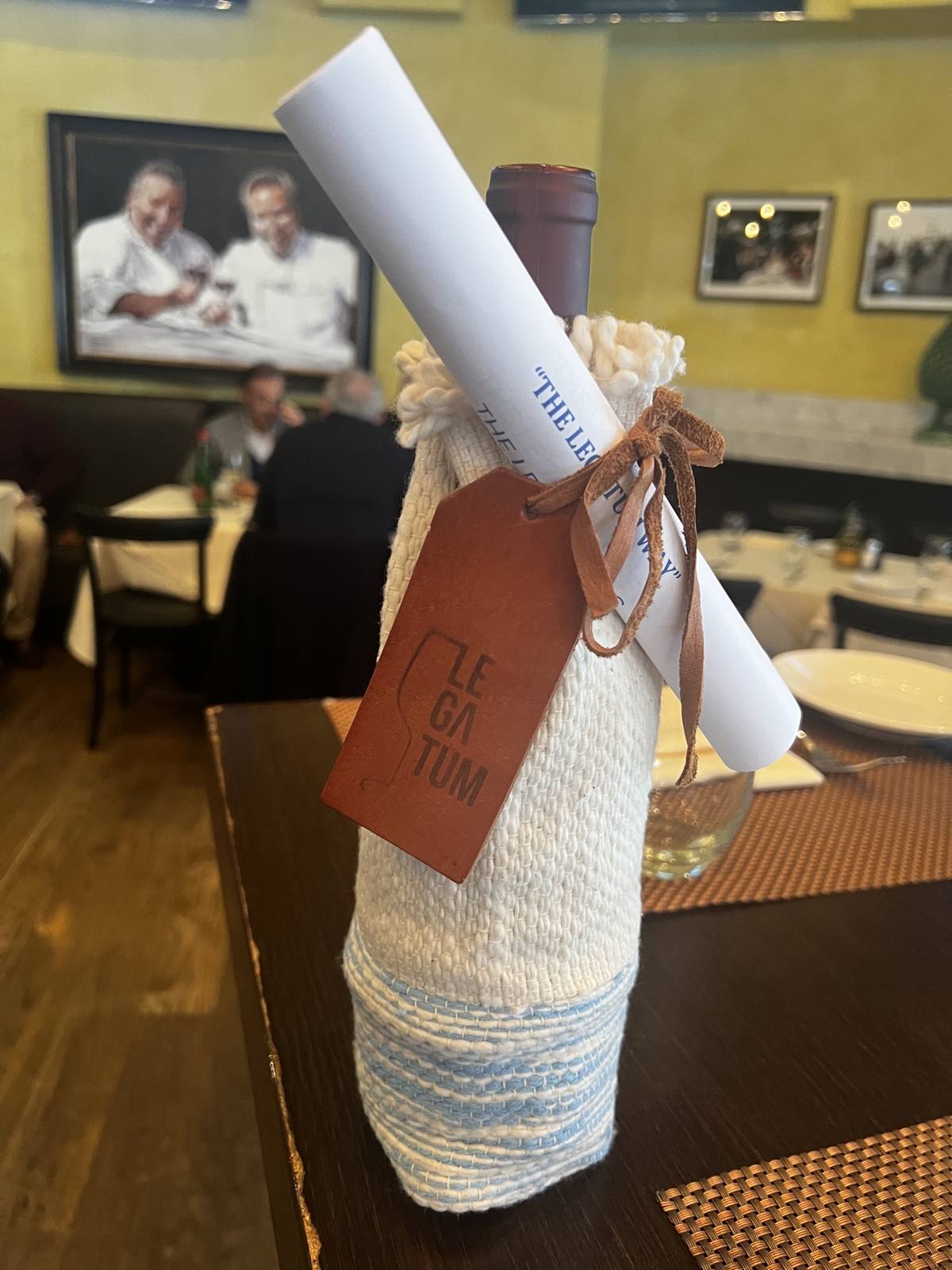 Legatum bottle dressed in its cream and blue hand-woven sleeve with embossed leather tag at Via Alloro