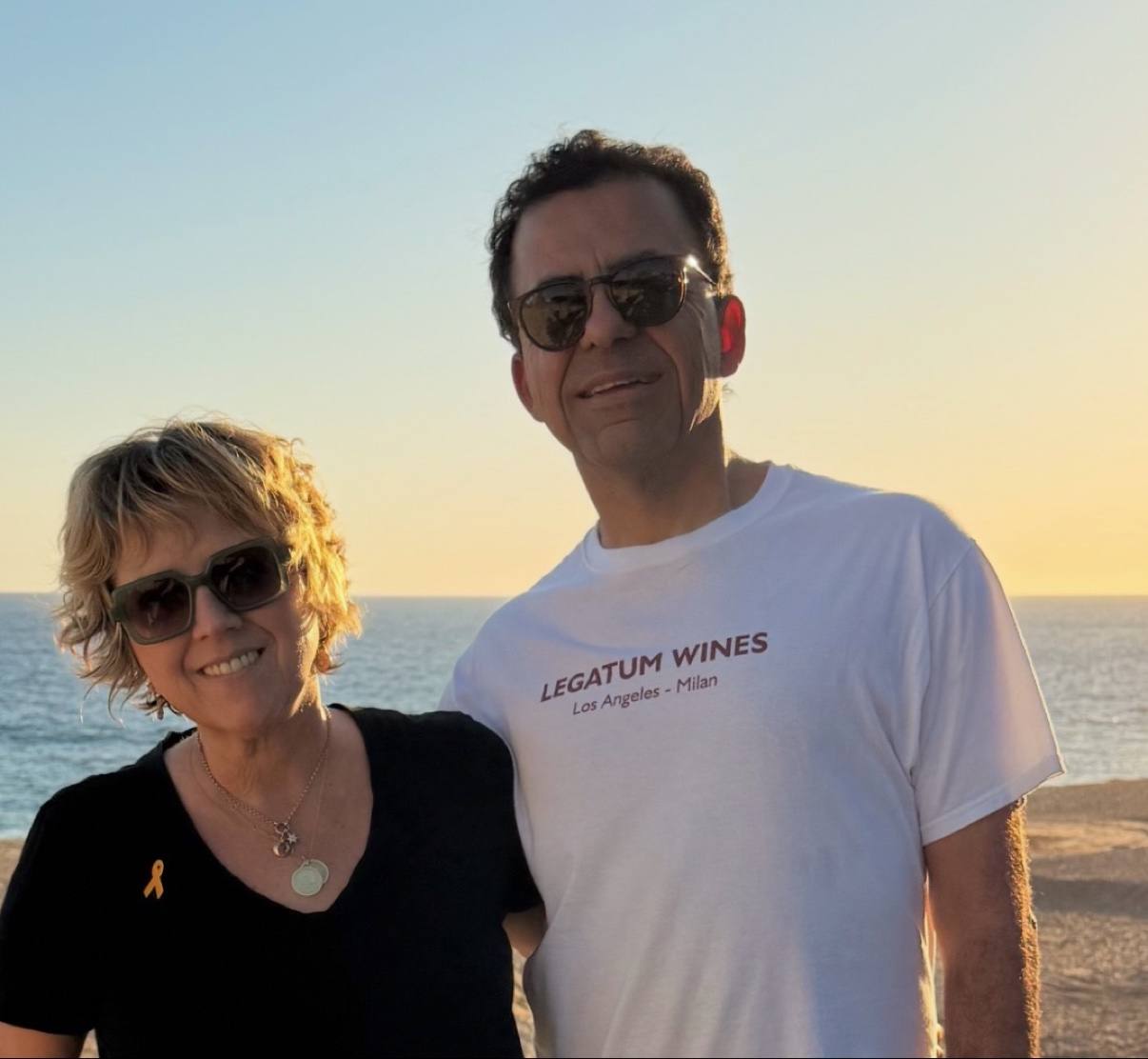 Guillermo Seta and his wife together at the beach at sunset, with Guillermo wearing his Legatum Wines Los Angeles–Milan shirt